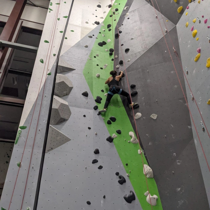 Child rock climbing on indoor wall with green and gray sections at climbing gym.