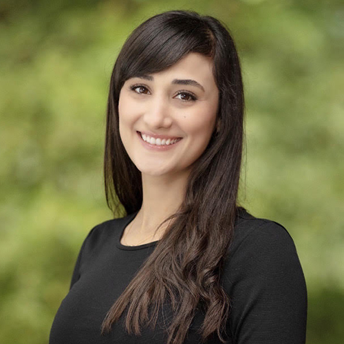 Professional headshot of smiling woman with long dark hair against blurred green background.