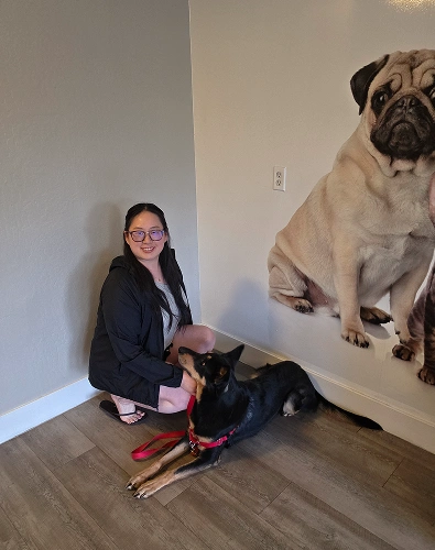 Woman crouching beside large dog mural in dental office interior.