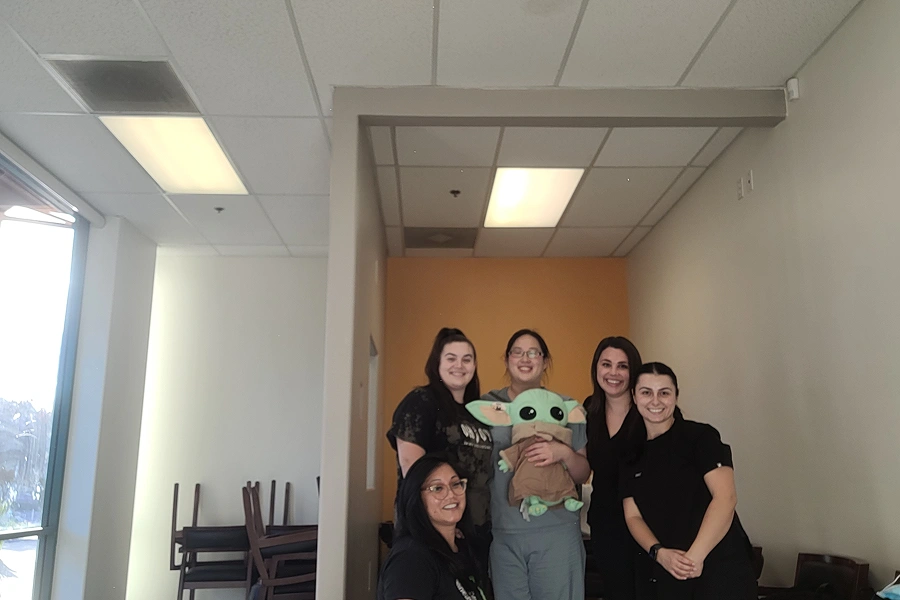 Team of dental professionals posing together in modern office hallway with fluorescent lighting.