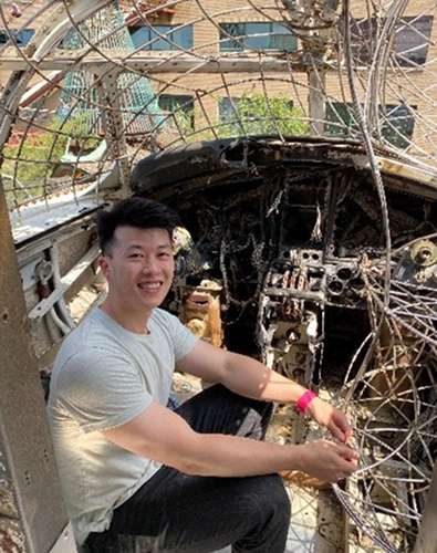 Young man holding dental equipment inside vehicle with tree branches visible through windshield.