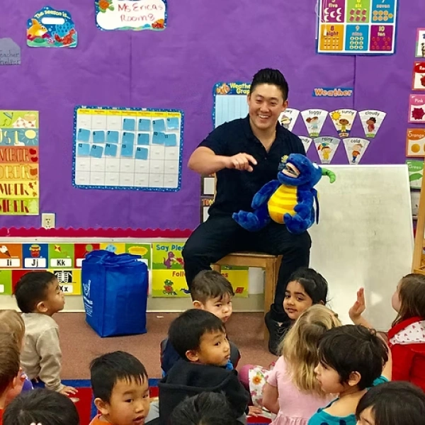 Pediatric dentist demonstrating dental care to young children in colorful classroom setting.