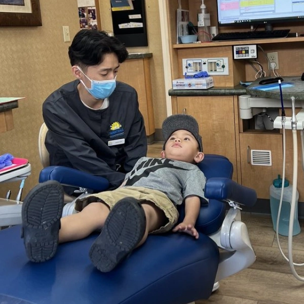 Pediatric dentist examining young child patient in dental office treatment chair.