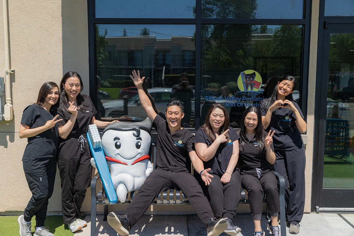 Clinic staff smiling and posing together outdoors around a friendly, caped tooth mascot character.