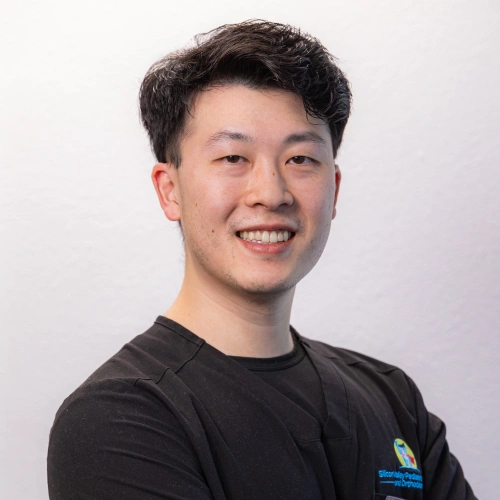 Professional headshot of Dr. Aaron Wong smiling in black scrubs against a white background.