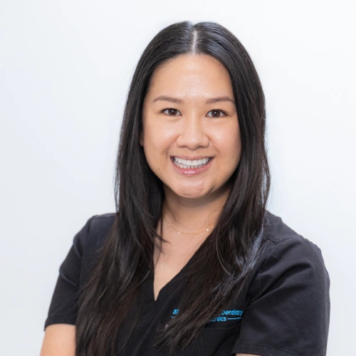 Professional headshot of Dr. Adrienne Nguyen smiling with long dark hair, wearing black scrubs against a white background.