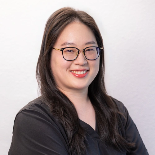 Professional headshot of Dr. Ariel Tsao smiling with glasses and long dark hair, wearing black scrubs against a white background.