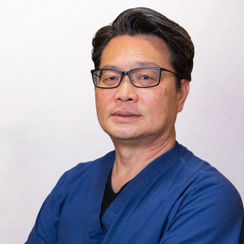 Professional headshot of Dr. Louis Tieu wearing glasses and blue scrubs against a white background.