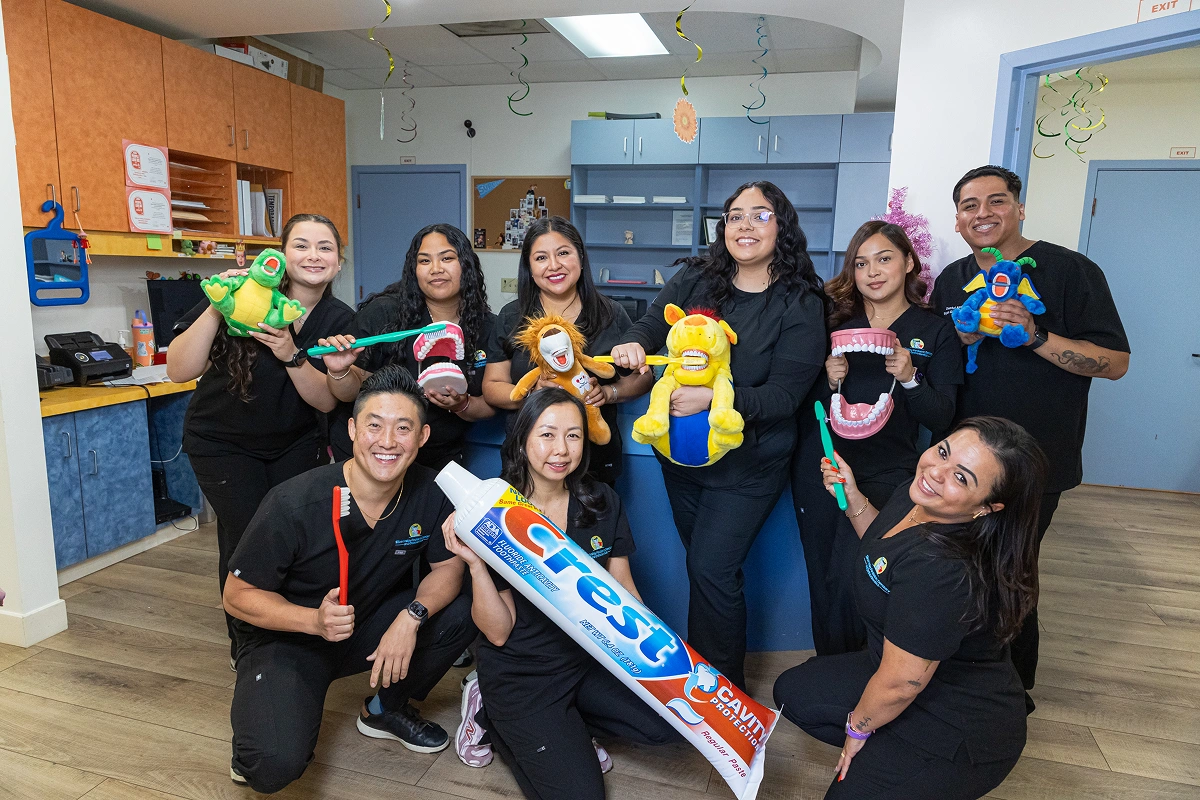 Dental staff members posing playfully inside the clinic while holding giant plush toys, dental teaching models, and a massive toothpaste tube.