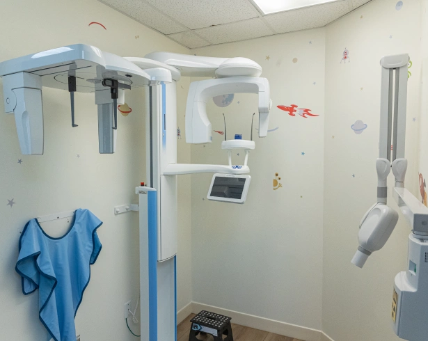 A modern dental panoramic X-ray machine standing in an examination room with walls decorated with child-friendly outer space stickers.