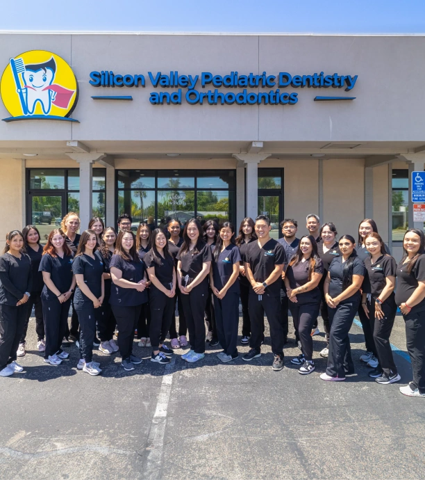 A large group of dental professionals posing together outside the entrance of Silicon Valley Pediatric Dentistry and Orthodontics.
